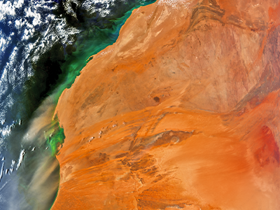 This image encompasses all of the letters in  the PACE acronym. Blooms of phytoplankton (P) are seen as green colors off the coast. Red dust aerosols (A) blow from western Africa over the Atlantic Ocean that is dotted with clouds (C). Minerals carried within the dust deliver key nutrients such as iron to sustain life at the base of the ocean ecosystem (E). Credit: NASA