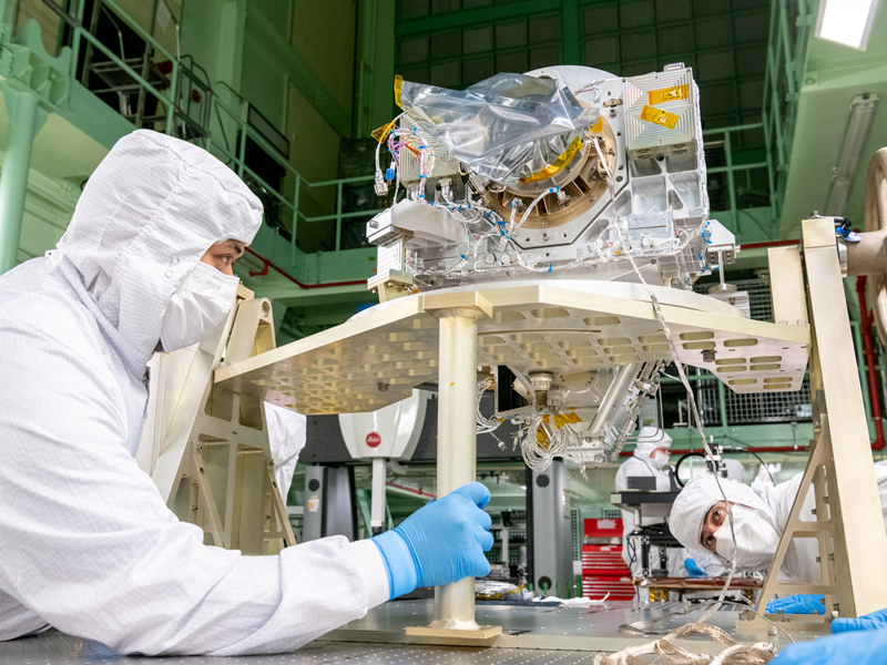 Mechanical technician Daniel Dizon stabilizes the Ocean Color Instrument Optical Module after a rotation for additional integration activities as mechanical engineer Michael Mulloney observes. Credit: Mellos, Katherine