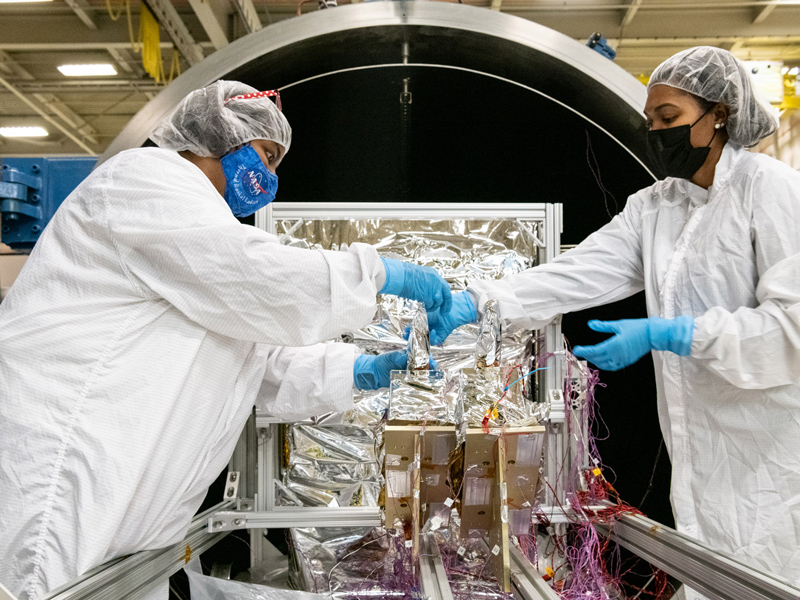Paula Cain and Aldine Joseph-Pierre apply thermal blanketing to the Ocean Color Instrument Loop Heat Pipes (LHP) prior to thermal vacuum testing. Credit: Mellos, Katherine