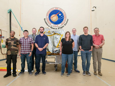 The GSFC environmental testing team poses with the bagged Ocean Color Instrument in the acoustic chamber prior to testing. Credit: Stover, Desiree
