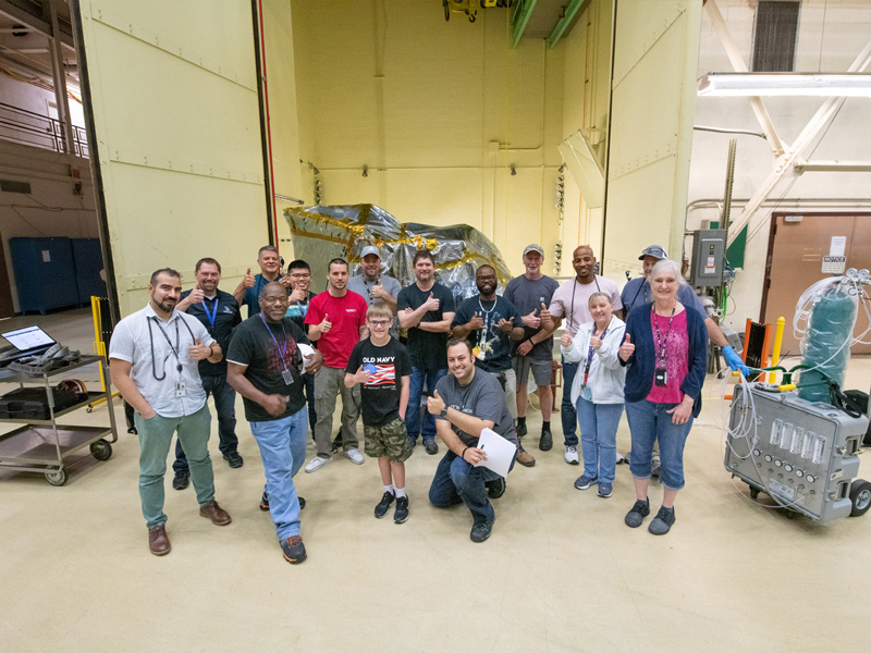 Ocean Color Instrument mechanical team poses with the bagged instrument behind them after a successful environmental testing campaign. Credit: Stover, Desiree