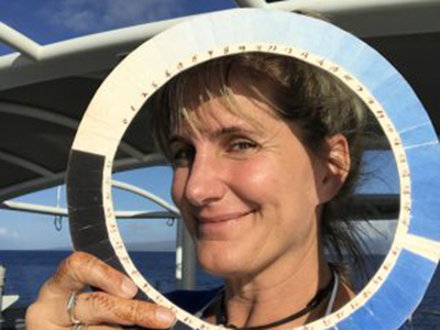 Artist at Sea Kirsten Carlson poses with a replica of a cyanometer, a tool used to measure ’blueness’, or the color intensity of blue sky. Credit: Schmidt Ocean Institute